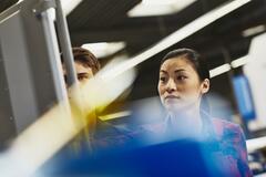 Male and female watching a board. Inside. Primary color blue. Secondary color yellow.