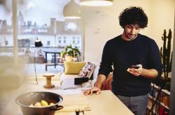 Man standing next to the kitchen counter top, looking at his phone.