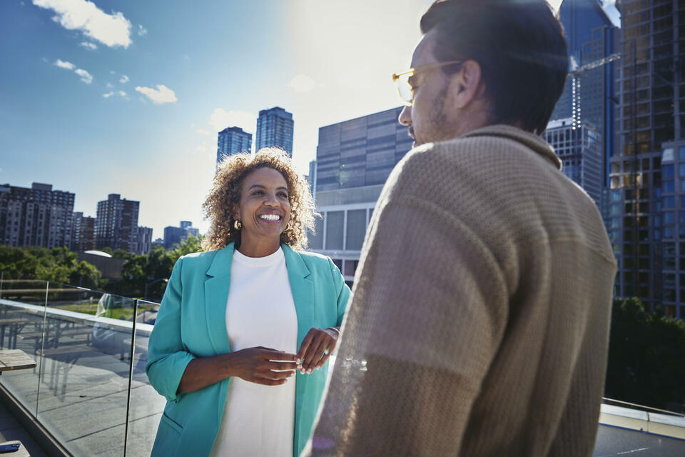 Female and male with glasses, standing outside on a balcony, talking